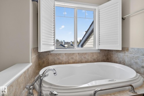 Soaking tub featuring a tiled surround, window with white plantation shutters, and polished chrome fixtures - 34 3003 34 Avenue, Edmonton, AB - Indoor Photo Showing Bathroom