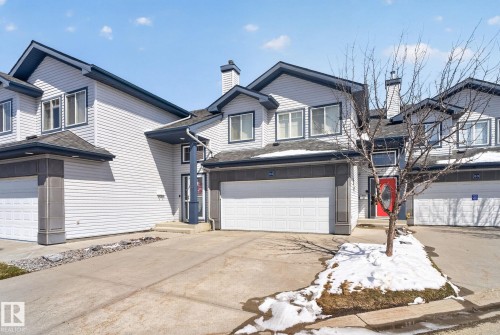 Two-story townhouse exterior with light siding, dark trim, an attached garage, a red entry door, and a chimney feature - 34 3003 34 Avenue, Edmonton, AB - Outdoor With Facade