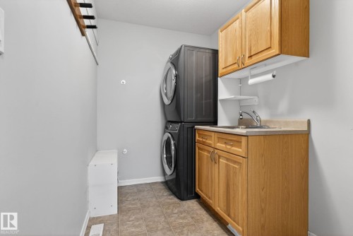 Utility area featuring stacked washer and dryer, light wood-finish cabinetry, a utility sink with a chrome faucet, and tiled flooring - 34 3003 34 Avenue, Edmonton, AB - Indoor Photo Showing Laundry Room