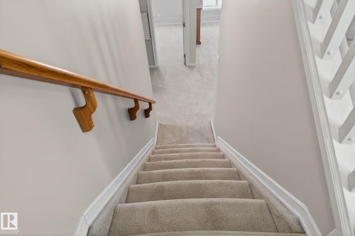 Staircase with carpeted treads and risers, featuring a natural wood handrail and white balusters - 34 3003 34 Avenue, Edmonton, AB - Indoor Photo Showing Other Room