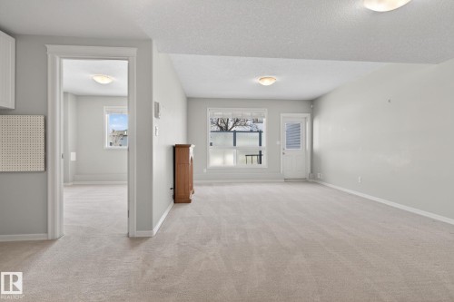 Spacious carpeted room featuring a window, an exterior door, and ceiling-mounted light fixtures - 34 3003 34 Avenue, Edmonton, AB - Indoor Photo Showing Other Room