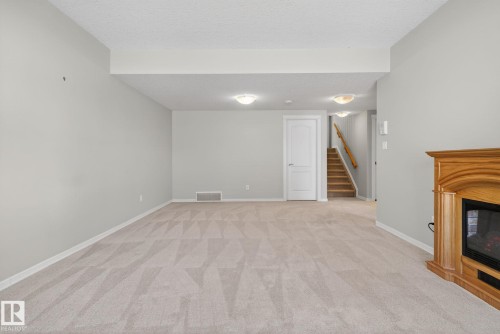 Spacious carpeted room featuring a natural wood fireplace with a black insert, light gray walls, white trim, and recessed lighting - 34 3003 34 Avenue, Edmonton, AB - Indoor Photo Showing Other Room With Fireplace