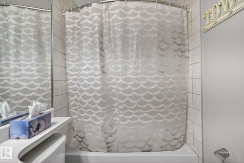 White tiled shower surround with a built-in tub, curved shower rod, and chrome fixtures - 34 3003 34 Avenue, Edmonton, AB - Indoor Photo Showing Bathroom