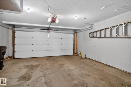 Spacious garage featuring a sectional overhead door, automatic opener, ceiling-mounted lighting, and concrete flooring - 34 3003 34 Avenue, Edmonton, AB - Indoor Photo Showing Garage