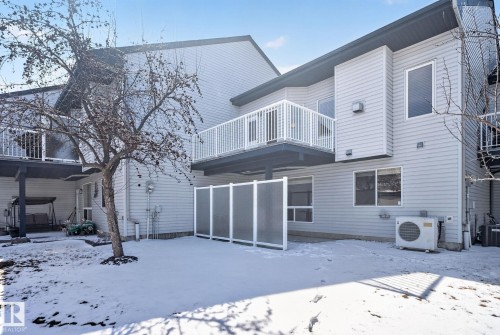 Rear exterior showcasing light gray horizontal siding, an upper-level balcony with white railings, and a lower-level concrete patio with a translucent privacy screen - 34 3003 34 Avenue, Edmonton, AB - Outdoor With Balcony