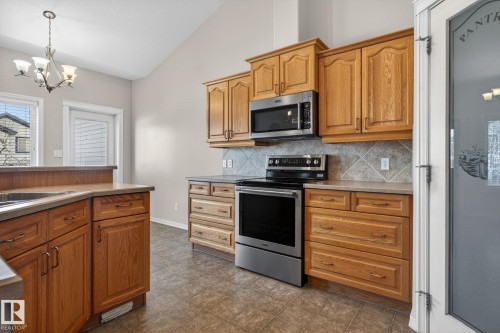 Kitchen featuring light wood cabinetry, stainless steel appliances, tile flooring, and a pantry with a frosted glass door - 34 3003 34 Avenue, Edmonton, AB - Indoor Photo Showing Kitchen