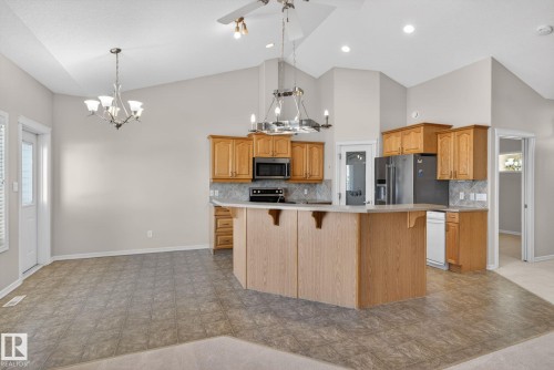 Open-concept kitchen featuring light-tone wood cabinetry, a breakfast bar, and a patterned tile backsplash - 34 3003 34 Avenue, Edmonton, AB - Indoor Photo Showing Kitchen