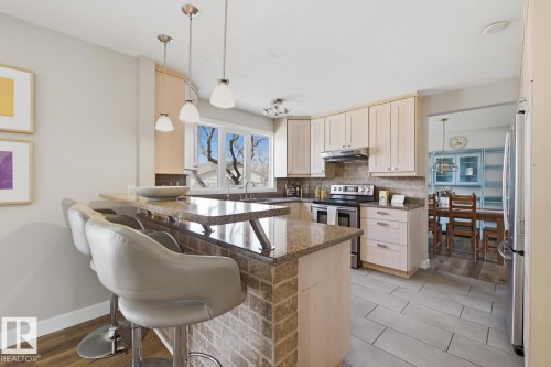 Spacious kitchen featuring light wood cabinetry, stone countertops, a brick-patterned island base, stainless steel appliances, and large windows - 17604 85 Avenue, Edmonton, AB - Indoor Photo Showing Kitchen With Upgraded Kitchen