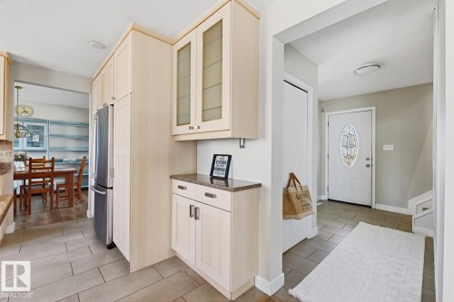 Kitchen cabinetry featuring light wood-finish doors, glass-front upper cabinets, and a polished stone countertop - 17604 85 Avenue, Edmonton, AB - Indoor