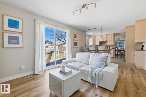 Open-concept living space featuring wood-finish flooring, a sliding glass door to the backyard, track lighting, and a kitchen with light wood cabinetry, a breakfast bar, and pendant lighting - 17604 85 Avenue, Edmonton, AB - Indoor Photo Showing Living Room