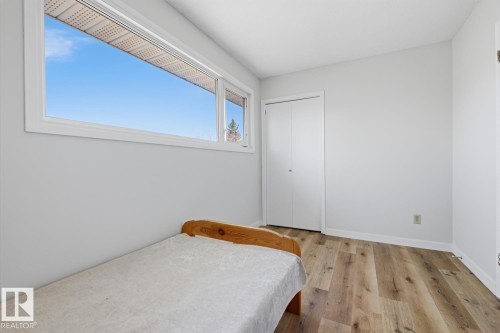 Room featuring a wide window with white trim, wood-finish flooring, a bi-fold closet, and light-colored wall paint - 17604 85 Avenue, Edmonton, AB - Indoor Photo Showing Bedroom
