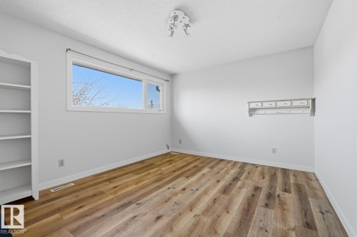 Spacious interior room featuring wood-finish flooring, a large window, built-in shelving, and a decorative wall-mounted shelf with hooks - 17604 85 Avenue, Edmonton, AB - Indoor Photo Showing Other Room