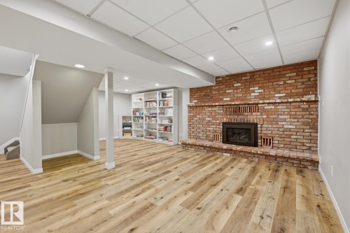 Spacious room featuring wood-finish flooring, a brick-surround fireplace, recessed lighting, built-in shelving, and a drop ceiling - 17604 85 Avenue, Edmonton, AB - Indoor With Fireplace