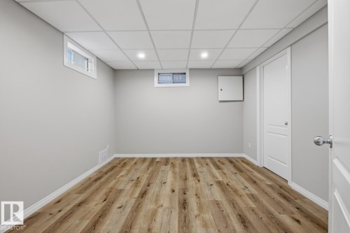 Spacious room featuring wood-finish flooring, light grey walls, and a white grid ceiling with recessed lighting - 17604 85 Avenue, Edmonton, AB - Indoor