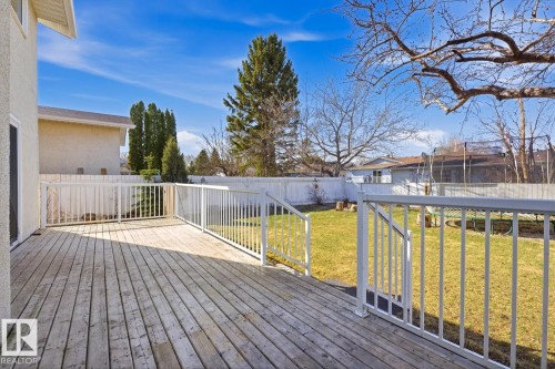Spacious wood deck with white railings overlooks a fenced backyard featuring a green lawn and mature trees - 17604 85 Avenue, Edmonton, AB - Outdoor With Deck Patio Veranda