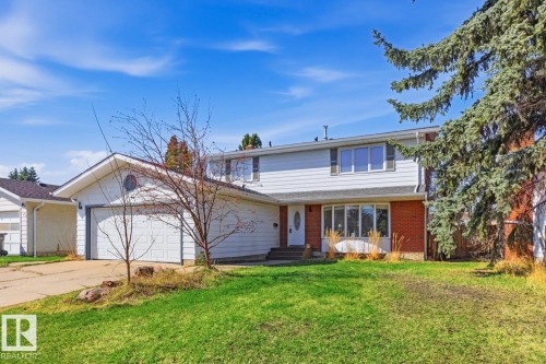 Two-story exterior with white siding and brick accents, featuring a two-car garage with a circular window, a bay window, and mature evergreen trees - 17604 85 Avenue, Edmonton, AB - Outdoor