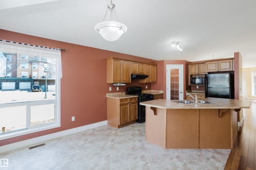 Kitchen featuring an island with double sink, wood cabinetry, and black appliances including a range and refrigerator - 9 102 Bridgeport Crossing, Leduc, AB - Indoor Photo Showing Kitchen With Double Sink