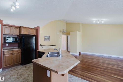 Kitchen featuring a double basin stainless steel sink, wood-finish cabinetry, and tiled flooring - 9 102 Bridgeport Crossing, Leduc, AB - Indoor Photo Showing Kitchen With Double Sink