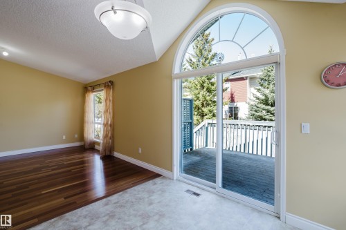 Spacious room featuring vaulted ceilings, a large arched window, and a sliding glass door opening to a wooden deck - 9 102 Bridgeport Crossing, Leduc, AB - Indoor Photo Showing Other Room