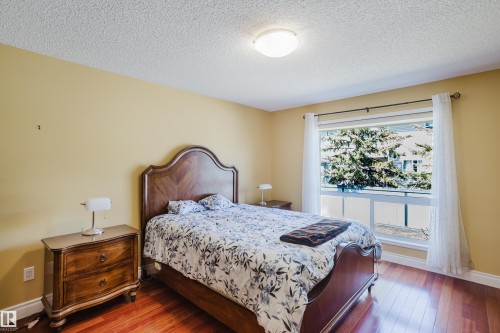 Bedroom featuring warm yellow walls, wood-finish flooring, and a large window with white trim - 9 102 Bridgeport Crossing, Leduc, AB - Indoor Photo Showing Bedroom