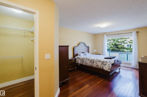 Bedroom featuring wood-finish flooring, a broad window with white curtains, and a ceiling-mounted light fixture - 9 102 Bridgeport Crossing, Leduc, AB - Indoor Photo Showing Bedroom
