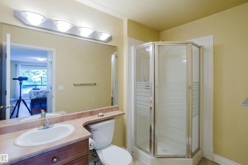 Bathroom featuring a corner shower enclosure with frosted glass panels, a vanity with an integrated sink, a rectangular mirror, overhead lighting, and a toilet - 9 102 Bridgeport Crossing, Leduc, AB - Indoor Photo Showing Bathroom