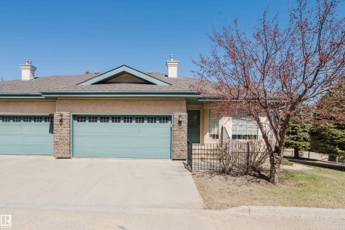Cream stucco exterior with two teal garage doors featuring window inserts - 9 102 Bridgeport Crossing, Leduc, AB - Outdoor