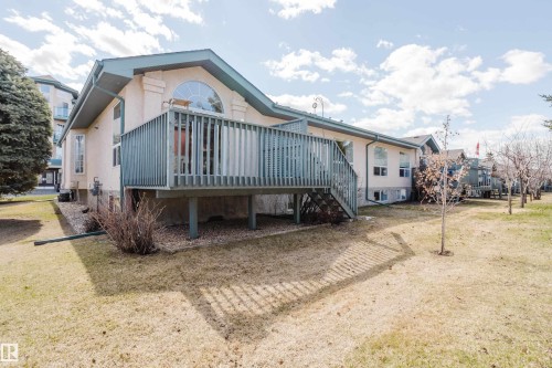 Rear exterior featuring a raised wooden deck with railings and stairs, a large arched window, multiple lower-level windows, and a manicured lawn - 9 102 Bridgeport Crossing, Leduc, AB - Outdoor With Deck Patio Veranda