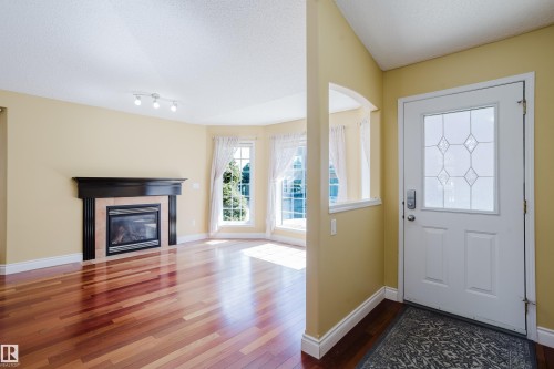 Foyer with a white entry door featuring window to let in more light, leading to a living area with wood-finish flooring - 9 102 Bridgeport Crossing, Leduc, AB - Indoor Photo Showing Living Room With Fireplace