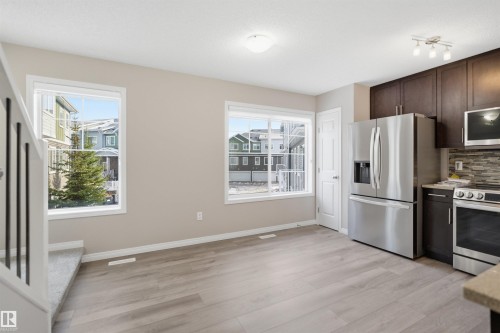 Kitchen and dining area featuring light wood-finish flooring, ample natural light from multiple windows, dark wood cabinetry, a mosaic tile backsplash, and stainless steel appliances - 33 7385 Edgemont Way Nw, Edmonton, AB - Indoor Photo Showing Kitchen