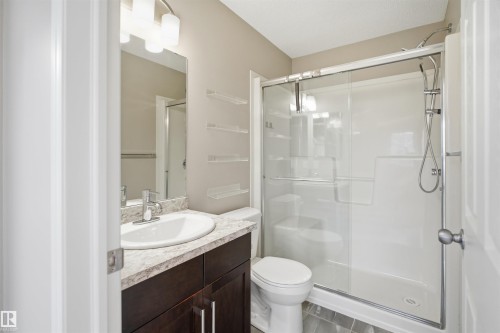 Bathroom featuring a dark wood-finish vanity with a light-toned countertop, an undermount sink, and a mirrored wall - 33 7385 Edgemont Way Nw, Edmonton, AB - Indoor Photo Showing Bathroom