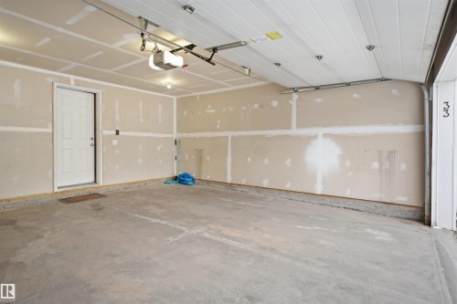 Spacious two-car garage featuring a concrete floor, an overhead garage door, interior access door, and an automatic garage door opener - 33 7385 Edgemont Way Nw, Edmonton, AB - Indoor Photo Showing Garage