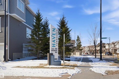 Modern townhome community featuring a distinctive entrance sign, mature evergreen landscaping, and multi-story residences with varied siding textures - 33 7385 Edgemont Way Nw, Edmonton, AB - Outdoor