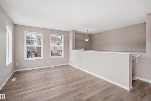 Open-concept room featuring wood-finish flooring, neutral wall paint, and multiple windows with white trim - 33 7385 Edgemont Way Nw, Edmonton, AB - Indoor Photo Showing Other Room