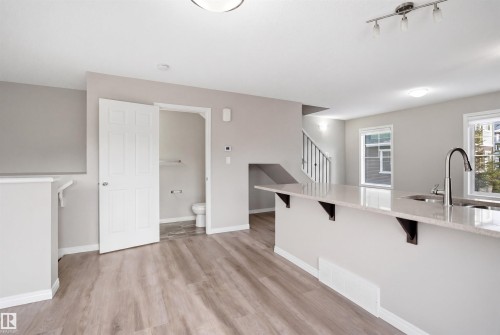 Open-concept living area with plank wood-finish flooring, a kitchen island with stone countertop, stainless steel sink with gooseneck faucet, two windows, and a staircase - 33 7385 Edgemont Way Nw, Edmonton, AB - Indoor
