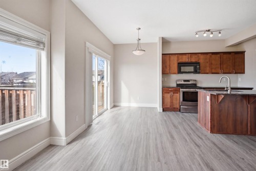 Open-concept living space featuring wood-finish flooring, a kitchen island with integrated sink, stainless steel appliances, and abundant natural light from a large window and sliding glass door - 19 15151 43 Street, Edmonton, AB - Indoor Photo Showing Kitchen