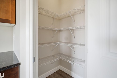 Walk-in pantry featuring multiple levels of wire shelving, light-toned wall paint, and wood-finish flooring with white baseboards - 19 15151 43 Street, Edmonton, AB - Indoor With Storage