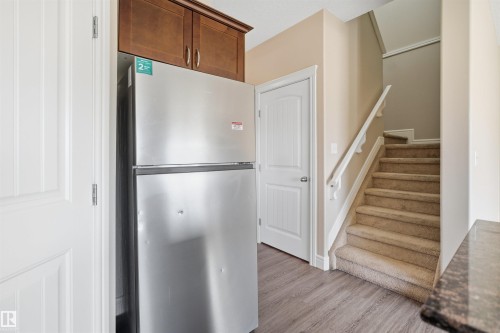 Stainless steel refrigerator with upper wood cabinetry, wood-finish flooring, and a carpeted staircase with white railing - 19 15151 43 Street, Edmonton, AB - Indoor Photo Showing Other Room
