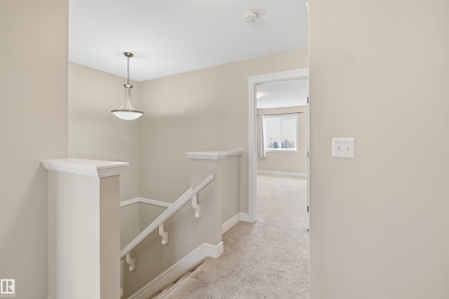 Upper-level landing featuring neutral-toned walls, a brushed nickel pendant light, white trim, a carpeted floor, and a staircase with white railings - 19 15151 43 Street, Edmonton, AB - Indoor Photo Showing Other Room