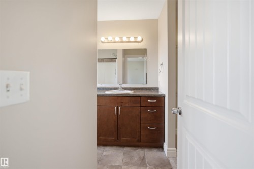 Bathroom vanity featuring a single basin sink, dark wood-finish cabinetry, a speckled countertop, and a wall-mounted mirror - 19 15151 43 Street, Edmonton, AB - Indoor
