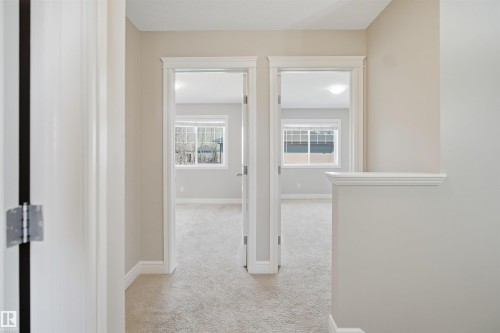 Hallway featuring light-toned carpeting, neutral wall paint, white trim, and two doorways leading into separate rooms - 19 15151 43 Street, Edmonton, AB - Indoor Photo Showing Other Room