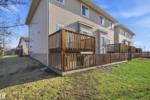 Rear exterior featuring light-colored horizontal siding, a two-story wooden deck, and a fenced yard with grass - 19 15151 43 Street, Edmonton, AB - Outdoor