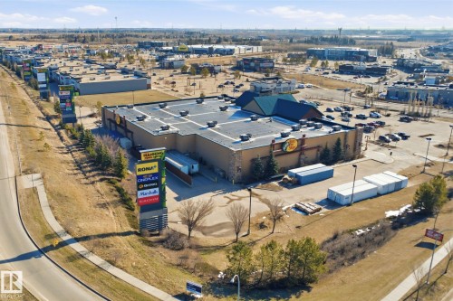 Commercial property featuring a large structure with a dark roof and stone-look facade, surrounded by a paved parking area - 19 15151 43 Street, Edmonton, AB - Outdoor With View