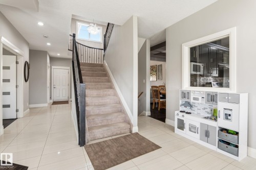 Foyer showcasing light tile flooring, a carpeted staircase with dark iron balusters, a large window providing natural illumination, recessed lighting, and a chandelier - 731 57 Street Sw, Edmonton, AB - Indoor Photo Showing Other Room