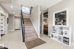 Foyer showcasing light tile flooring, a carpeted staircase with dark iron balusters, a large window providing natural illumination, recessed lighting, and a chandelier - 
