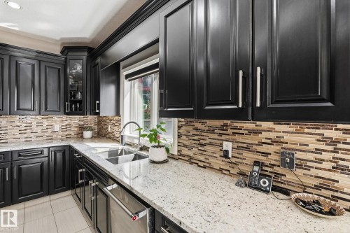 Kitchen featuring black cabinetry with brushed nickel hardware, light granite countertops, a stainless steel double basin sink with a gooseneck faucet, and a mosaic tile backsplash - 731 57 Street Sw, Edmonton, AB - Indoor Photo Showing Kitchen With Double Sink With Upgraded Kitchen