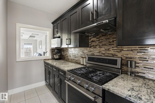 Modern kitchen featuring dark wood cabinetry with stainless steel hardware, granite countertops, and a full-height mosaic tile backsplash - 731 57 Street Sw, Edmonton, AB - Indoor Photo Showing Kitchen