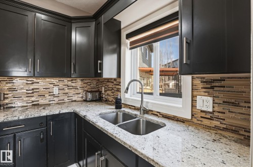 Kitchen featuring dark cabinetry, speckled countertops, a double basin stainless steel sink with a gooseneck faucet, and a mosaic tile backsplash - 731 57 Street Sw, Edmonton, AB - Indoor Photo Showing Kitchen With Double Sink