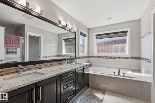 Dual sink vanity with dark wood-finish cabinetry, granite-style countertops, and a full-width mirror - 731 57 Street Sw, Edmonton, AB - Indoor Photo Showing Bathroom