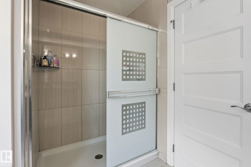 Tiled shower with sliding frosted glass enclosure and integrated shelf - 731 57 Street Sw, Edmonton, AB - Indoor Photo Showing Bathroom